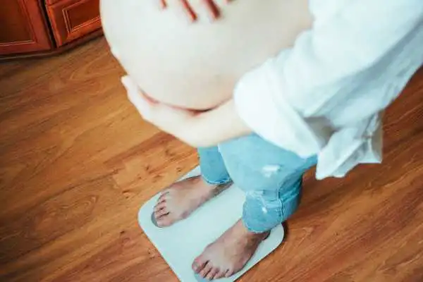 Image of woman weighing herself and experiencing weight gain through pregnancy Bletchley